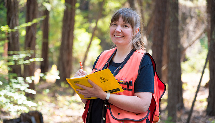Courtney Straight smiling at camera holding field notebook in a forest